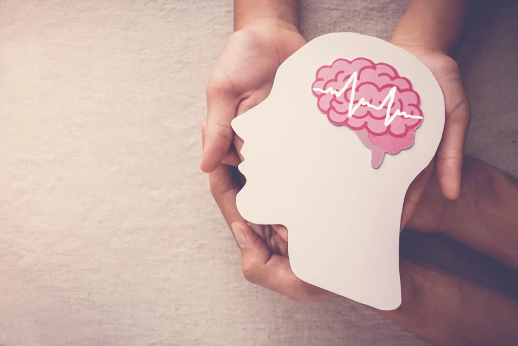 Hands holding a paper cutout of a human head with a brain illustration and heartbeat line.