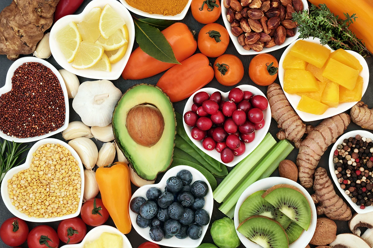 Assortment of fruits, vegetables, nuts, and grains in heart-shaped bowls on a dark background.